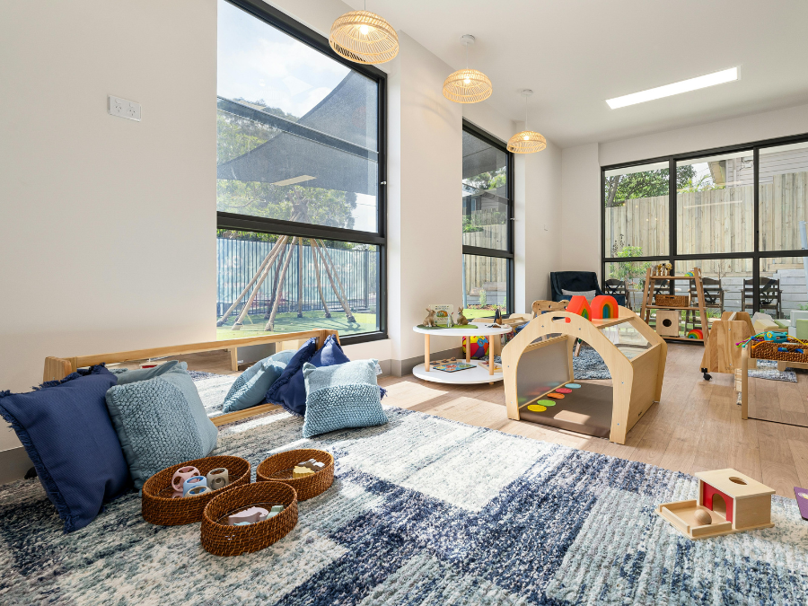 A bright, spacious playroom with natural light, colorful rugs, and wooden educational toys for children.