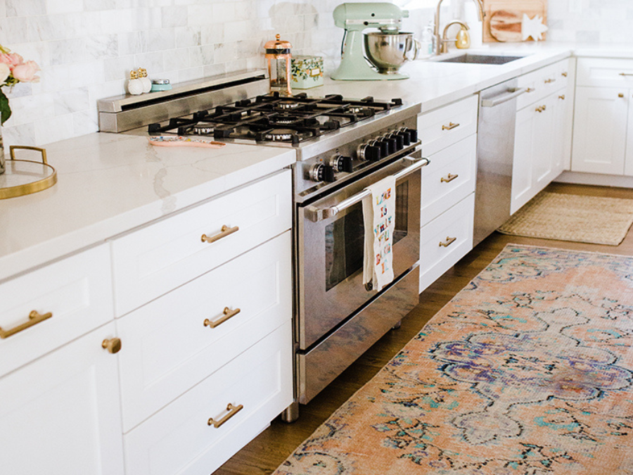 A classic kitchen with a washable patterned rug that enhances the white cabinetry and marble countertop.