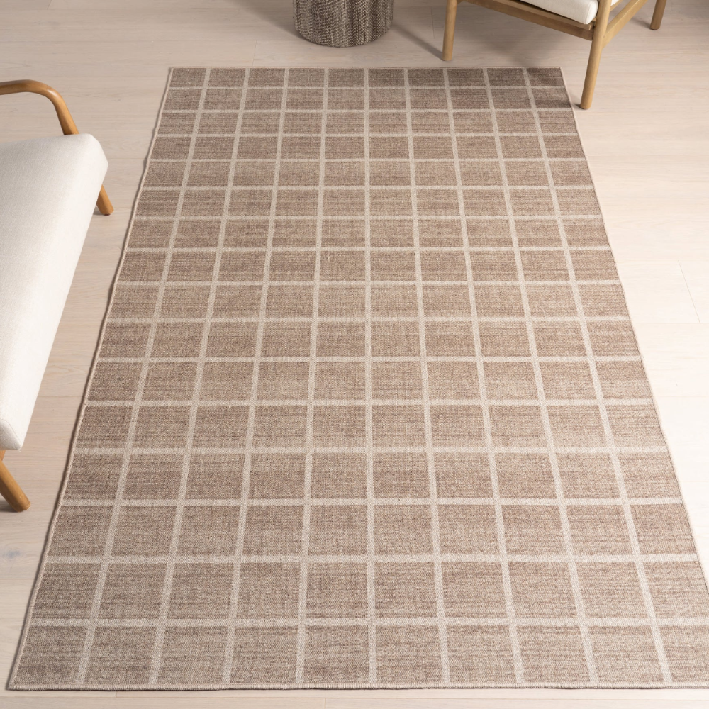 Beige grid Marcellus washable rug on light wood floor near modern chair.