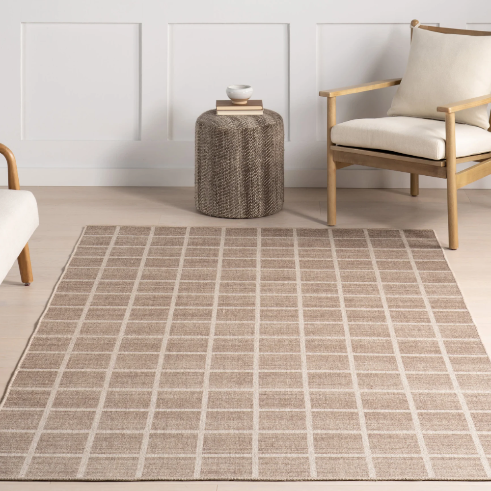 Beige grid Marcellus washable rug in modern living room with chair and woven stool